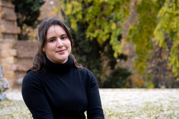 Happy girl smiling looking directly at camera .Portrait of a young European Caucasian woman wearing a black sweater outdoors on a park in autumn