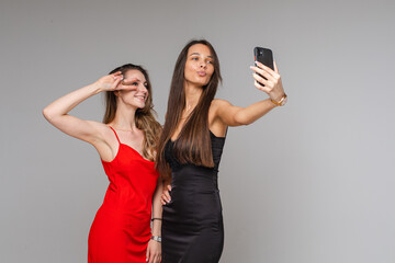 Pretty young girls bloggers wearing stylish dresses make selfie photography using phone posing on gray studio background