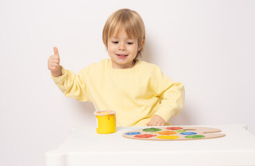 Inspired little boy at the table drawing with thumb up isolated on white