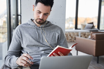 Man looking at the notebook and making notes while studying e learning at home