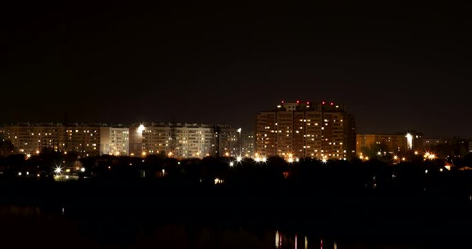 Illuminated brightly high-rise dwelling buildings in center of city under black sky without stars from evening till night time-lapse