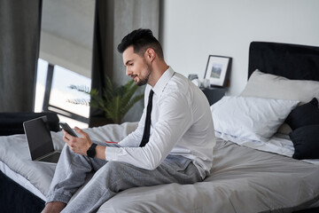 Man wearing suit sitting at the bed and looking at the smartphone screen