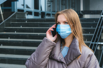 Young woman wearing a medical mask and talking to her mobile phone at the street