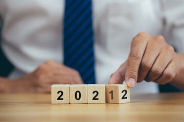 Businessman hand turning cube from 2021 to 2022 on wooden table.