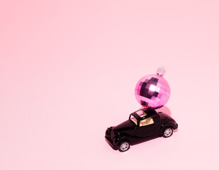 Classic black car delivering pink disco ball or Christmas bauble on the roof. Pastel pink...