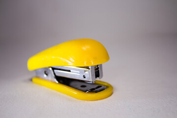 Yellow stapler for paper on a white background. - obrazy, fototapety, plakaty
