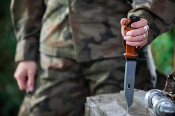 A woman in moro garb stabs a knife into a wooden crate. The soldier's equipment.