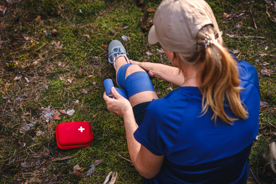 First aid after hiking accident. Injured hiker putting elastic bandage to her knee. Tendon problems or sprain knee during trekking in nature