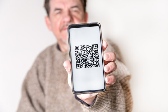 Adult man holding a smartphone with a QR-code. Virtual immunity passport or international certificate of vaccination. Contactless payment. Close-up - Powered by Adobe