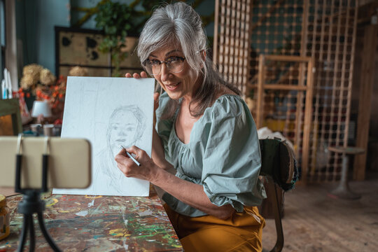 Lady in apron drawing portrait at the paper and smiling while explaining something
