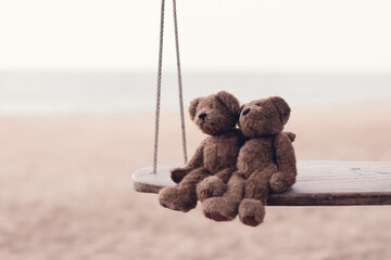 Two brown teddy bears so cute sitting on wooden swing looking to the sea in romantic moment. Concept of love and valentine's day or wedding, Cinematic tone.