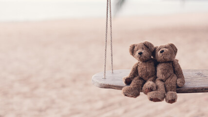 Two brown teddy bears so cute sitting on wooden swing looking to the sea in romantic moment. Concept of love and valentine's day or wedding, Cinematic tone.