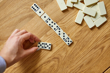 Top view of woman hand play white domino games on wooden table background with copy space, board game concept