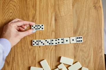 Top view of woman hand play white domino games on wooden table background with copy space, board game concept