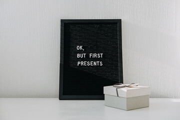Christmas minimal web banner with one Christmas gift box and black letter board with quote Ok but first presents. Festive Christmas letter board ideas and quotes.
