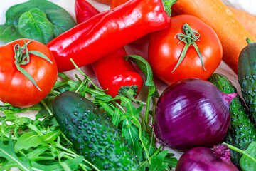 Fresh farm summer vegetables for salad: cucumbers, tomatoes, onions, peppers, arugula leaves in the kitchen on light background.