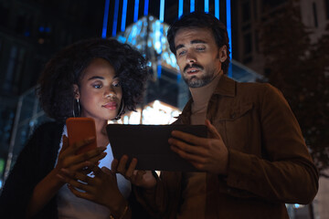 Man chatting about something with female colleague while standing at street with gadgets