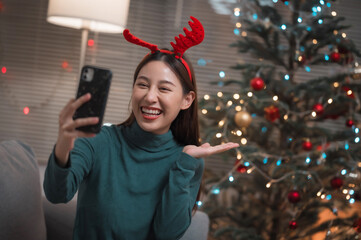 Happy smiling Asian woman video call via smartphone to celebrate with her friends or family during Christmas at home