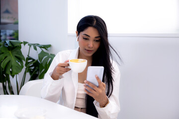 Young Indian ethnicity woman with long dark hair using smart phone and drinking coffee, lifestyle 