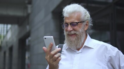Mature oldster laughing watching funny videos on smartphone, waiting bus or taxi