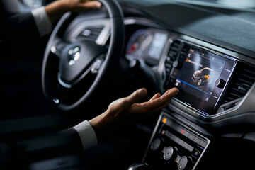 Close up of male person in stylish suit examining multimedia system of luxury car while choosing...