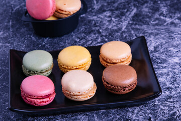Different macarons of different flavors on a black plate.