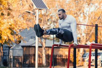 Muscular man hitting the frontal abs on parallel bars outside workout