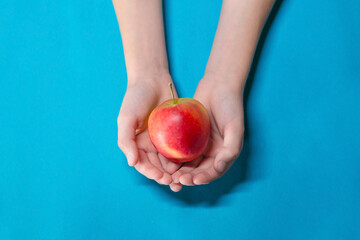 Human hands of a child holding ripe red apple over the table on a background