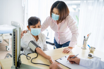 Obraz premium An elderly woman and an Asian woman come to see the doctor for a check-up at the hospital. Blood pressure is being checked. Wear a mask. The idea is to take care of elderly patients.