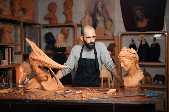 Serious carpenter at table with carved sculptures