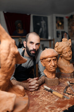 Serious carpenter at table with carved sculptures