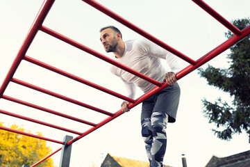 Young muscular man in dip position above the horizontal ladder outdoors workout