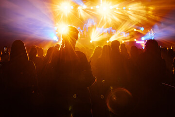 silhouette of the audience at a music concert. the happy audience dances and applauds their idols. bright multicolored spotlights illuminate the stage and the auditorium