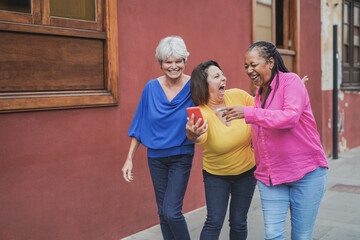 Multiracial senior women having fun in the city while using mobile phone