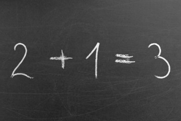 Easy school math equation 2 plus 1 is 3 written on a chalkboard by a student. School and education...