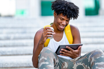 Smiling stylish young black man using tablet on street