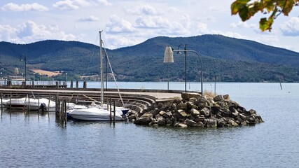 A pier made of concrete and boulders with boats moored in Lake Trasimeno (Umbria, Italy, Europe)