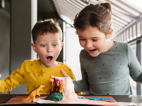 Amazed Children Playing With Dinosaur Toy And Plasticine Volcano