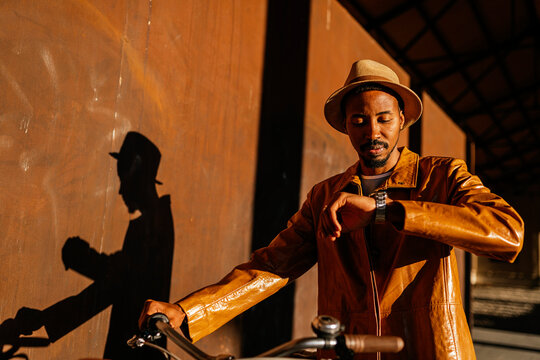 Black man with bicycle checking time on wristwatch