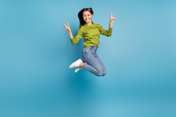Fototapeta na wymiar Photo of friendly cheerful lady show v-sign wear green shirt jeans sneakers isolated blue color background
