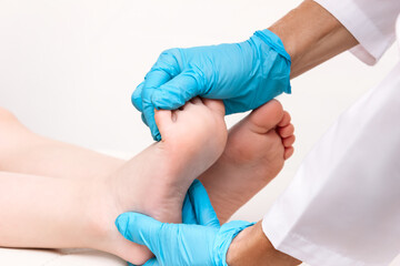 Examination of a child by an orthopedist. Close-up of female doctor's hands in blue medical gloves holding a kid's foot. Pathology of bone structures, flat feet, injury. Foot treatment