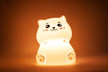 The baby cute kitten-shaped light night lamp with eyes and ears on the bedside table in the dark