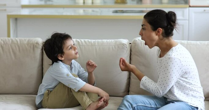 Young female qualified speech therapist work with little preschooler boy show correct spelling of words set pronunciation do phonetic exercises. Small child son imitate Indian mom in uttering sounds