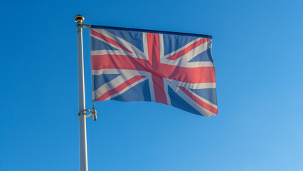 The flag of United Kingdom waving on wind on blue sky background. British union jack flag waggling in the wind.