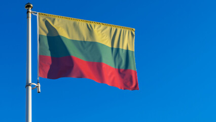 National flag of Lithuania on a flagpole in front of blue sky with sun rays and lens flare. Diplomacy concept.