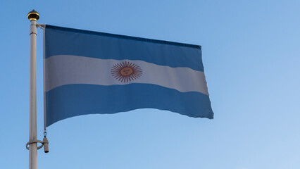 National flag of Argentina on a flagpole in front of blue sky with sun rays and lens flare. Diplomacy concept.