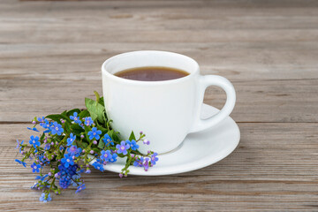 Happy mother's day greeting card; white cup of coffee or tea and bouquet of blue forget me not flowers on wooden background close up