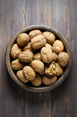 Walnuts in a plate on a brown wooden background. Nuts are a source of vegetable protein. Flat top view