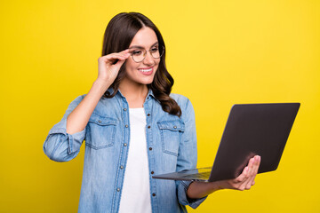 Photo of cute adorable young lady wear jeans shirt spectacles smiling looking modern device isolated yellow color background