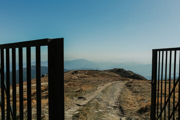 open door to new adventures, open metal slatted gates, unpaved road on the top of mountain ig going to nowhere down to horizon, blue sky 
